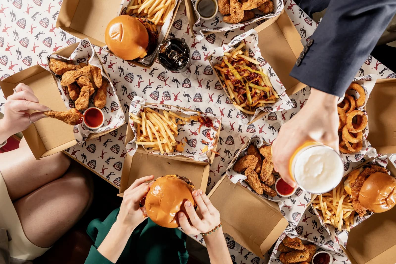 Friends sharing burgers, wings, fries and drinks at KG Sports Bar